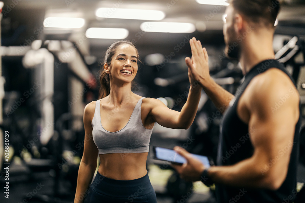 A happy woman is giving high five to her fitness trainer in a gym.
