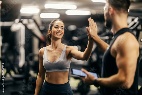 A happy woman is giving high five to her fitness trainer in a gym.