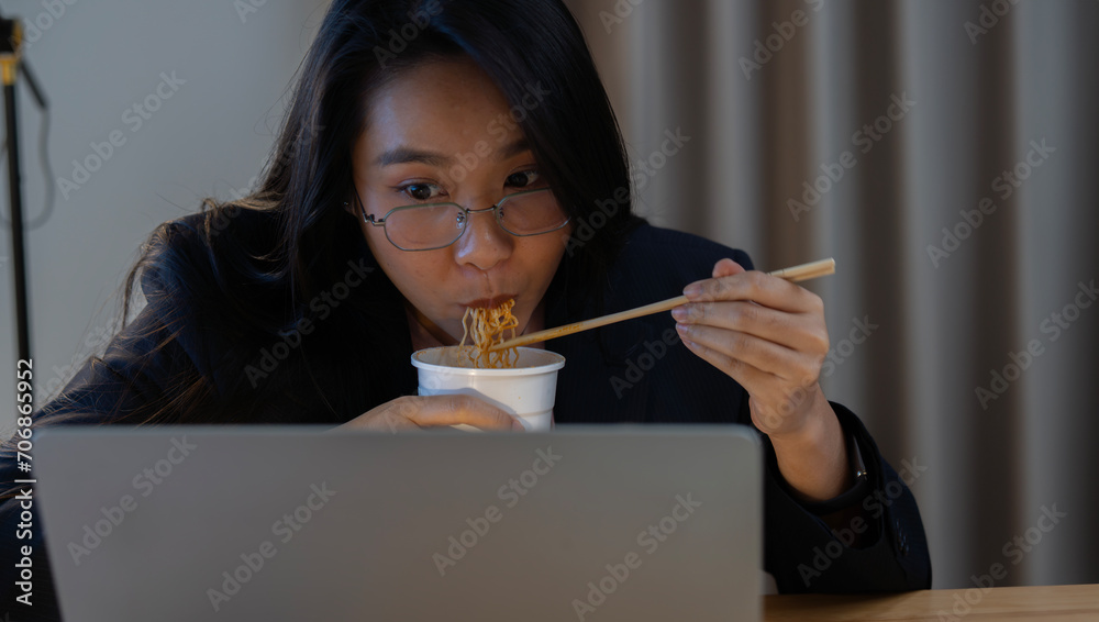 Female businesswoman, manager, employee is eating instant noodles during late work at midnight Female businesswoman, manager, employee is eating instant noodles during late work at midnight