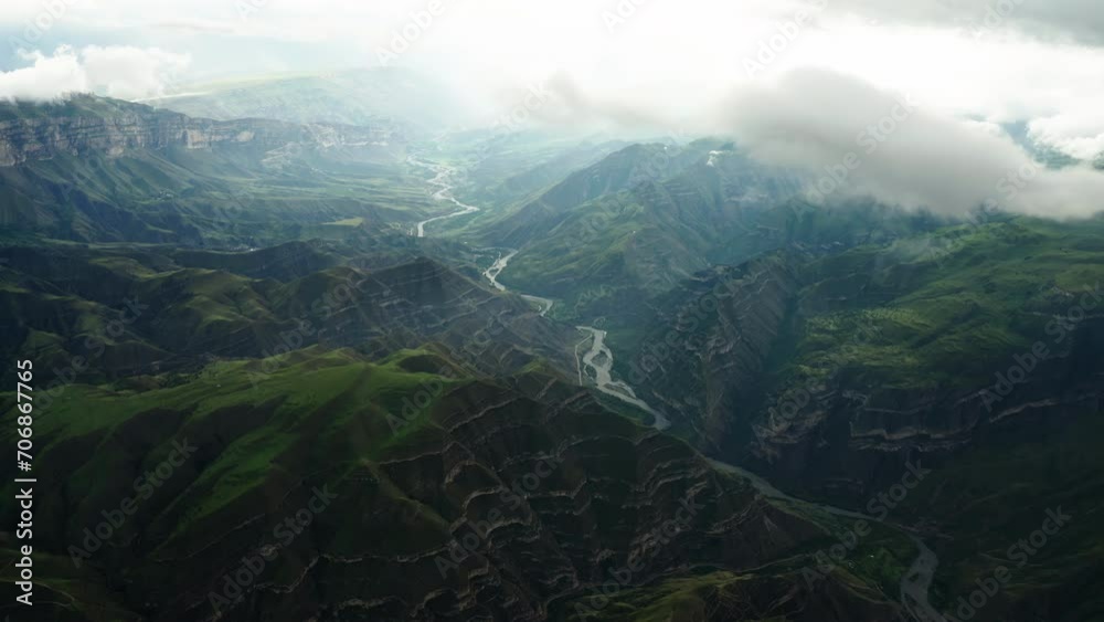 Sunlit River Winding Through Mountains. Sunlight breaks through clouds illuminating a river winding through a dramatic mountain range. Sunlit River Winding Through Mountains. Sunlight breaks through clouds illuminating a river winding through a dramatic mountain range.