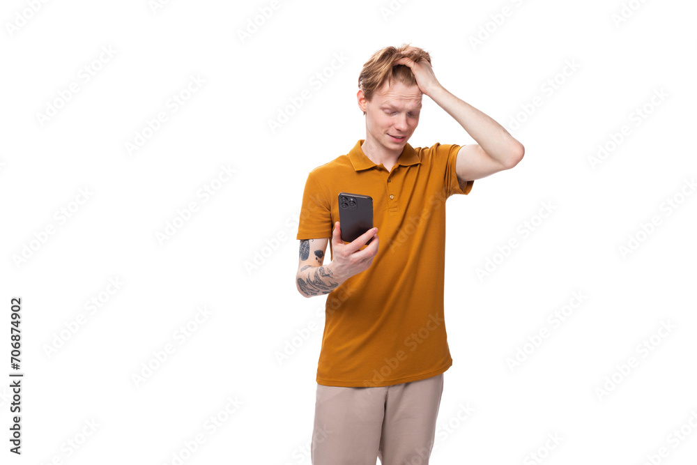 young handsome red-haired man with a haircut and a tattoo on his arm reads a message on the phone with excitement young handsome red-haired man with a haircut and a tattoo on his arm reads a message on the phone with excitement