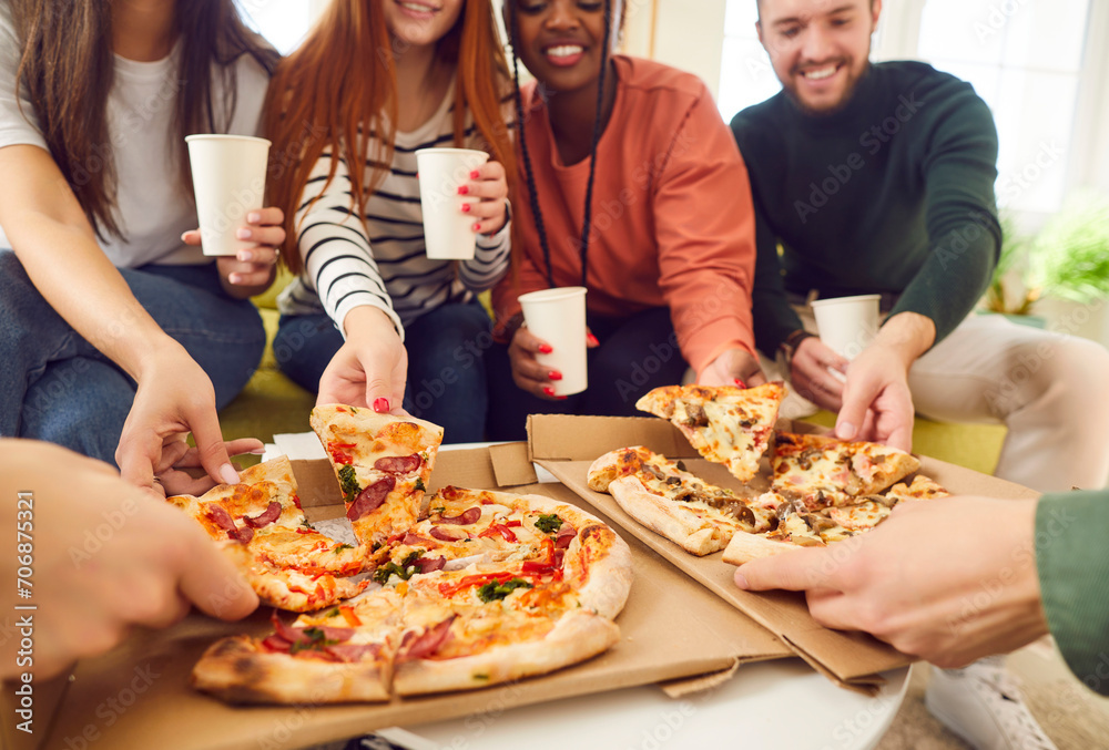 Happy smiling young people friends gathering in pizzeria or at home together eating tasty Italian food taking pizza slices from box enjoying party with cardboard cups in hands. Food delivery concept. Happy smiling young people friends gathering in pizzeria or at home together eating tasty Italian food taking pizza slices from box enjoying party with cardboard cups in hands. Food delivery concept.