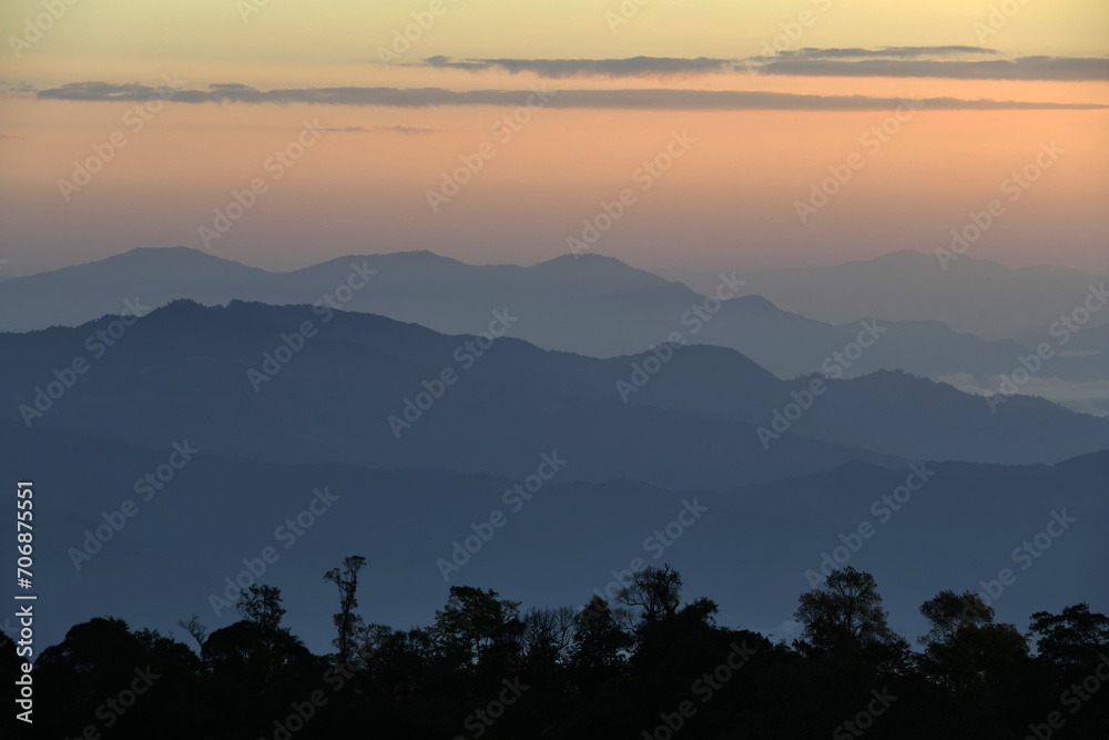 Colorful mountain range with tree line silhouette in foreground at sunset time
