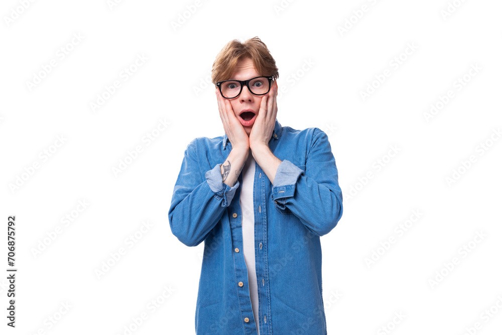 young joyful surprised red-haired guy dressed in a blue shirt wears glasses on a white background with copy space young joyful surprised red-haired guy dressed in a blue shirt wears glasses on a white background with copy space