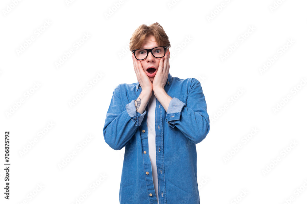 young joyful surprised red-haired guy dressed in a blue shirt wears glasses on a white background with copy space