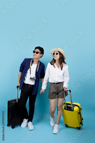 Happy Asian tourists with suitcases enjoying summer vacation together on blue background.