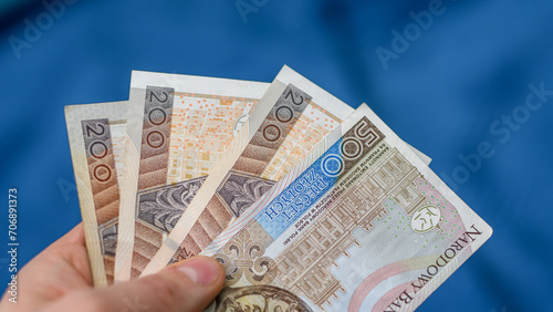 Polskie banknoty trzymane w dłoni, PLN na niebieskim tle
