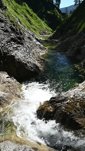 A small waterall of a mountain stream with a pond and clear water in summer sunlight, vertical shot photo