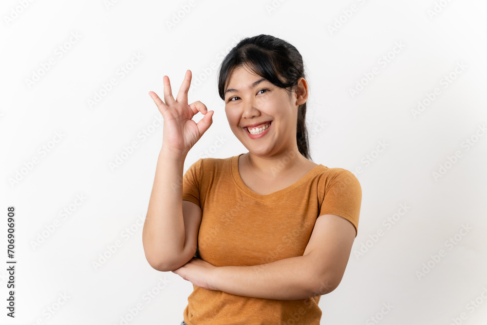 The cheerful young Asian woman smiling and showing the OK hand sign standing on white background. The cheerful young Asian woman smiling and showing the OK hand sign standing on white background.