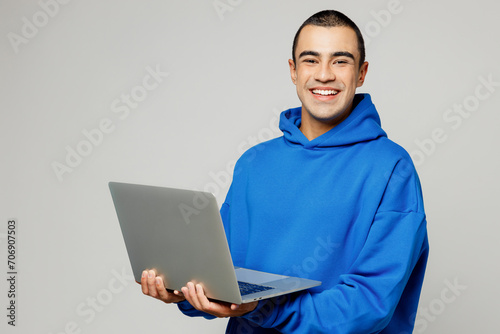 Side view young happy middle eastern IT man wear blue hoody casual clothes hold use work on laptop pc computer look camera isolated on plain solid white background studio portrait. Lifestyle concept.
