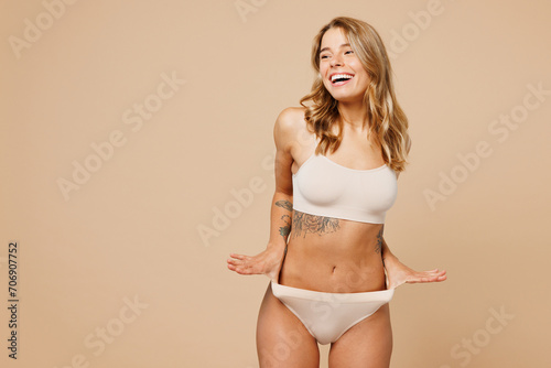 Photography Young nice lady woman with slim body perfect skin wear nude top bra lingerie stand hold hands on panties look aside on area isolated on plain pastel light beige background