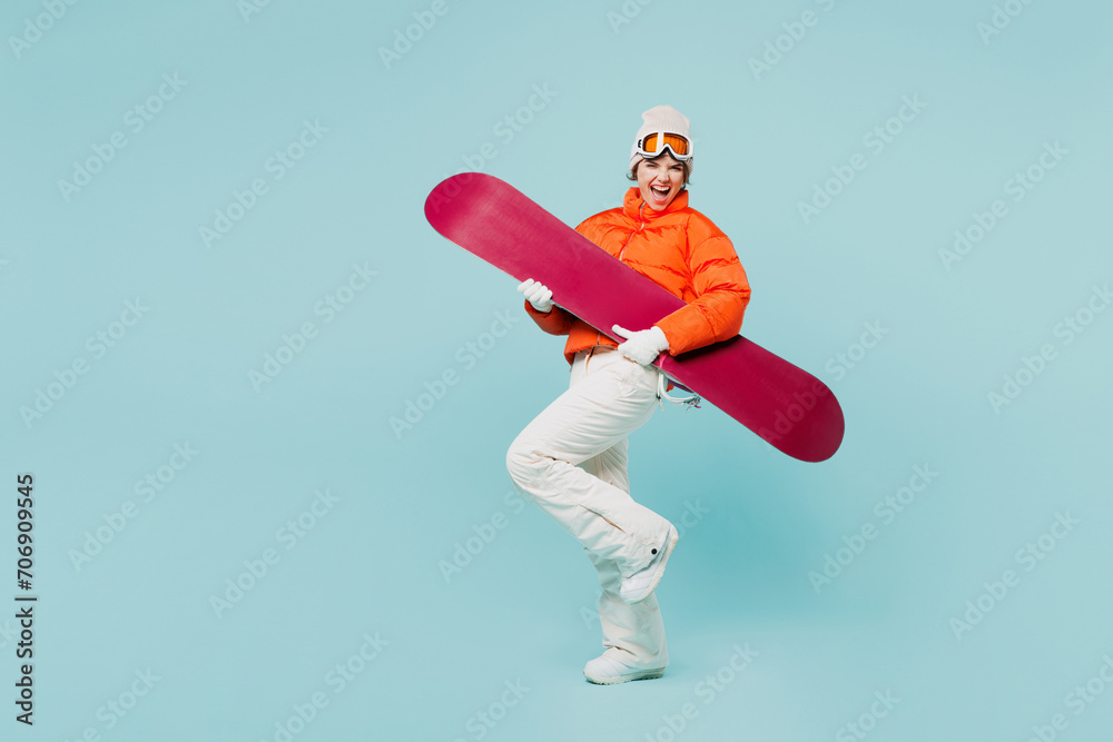 Full body young woman wears warm padded windbreaker jacket hat ski goggles mask hold snowboard pov play guitar travel rest spend weekend winter season in mountains isolated on plain blue background. Full body young woman wears warm padded windbreaker jacket hat ski goggles mask hold snowboard pov play guitar travel rest spend weekend winter season in mountains isolated on plain blue background.