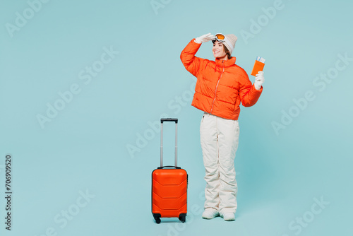 Traveler skier woman wearing padded windbreaker jacket ski goggles mask hold passport ticket bag isolated on plain blue background Tourist travel abroad in free time rest getaway. Air flight concept. #706909520
