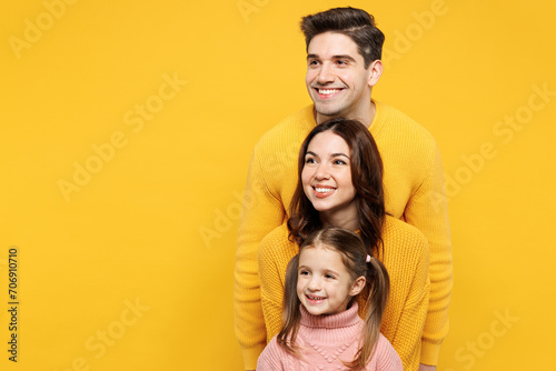 Young fun parents mom dad with child kid girl 7-8 years old wear pink knitted sweater casual clothes stand behind each other look aside on area isolated on plain yellow background. Family day concept. © ViDi Studio