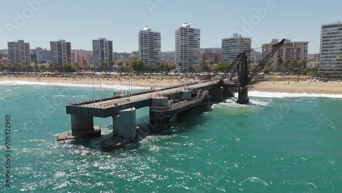 Aerial View Of Vergara Pier In Vina Del Mar With Hotel And Beach Coastline In Background. Pull Back Shot Over Turquoise Ocean Waters  photo