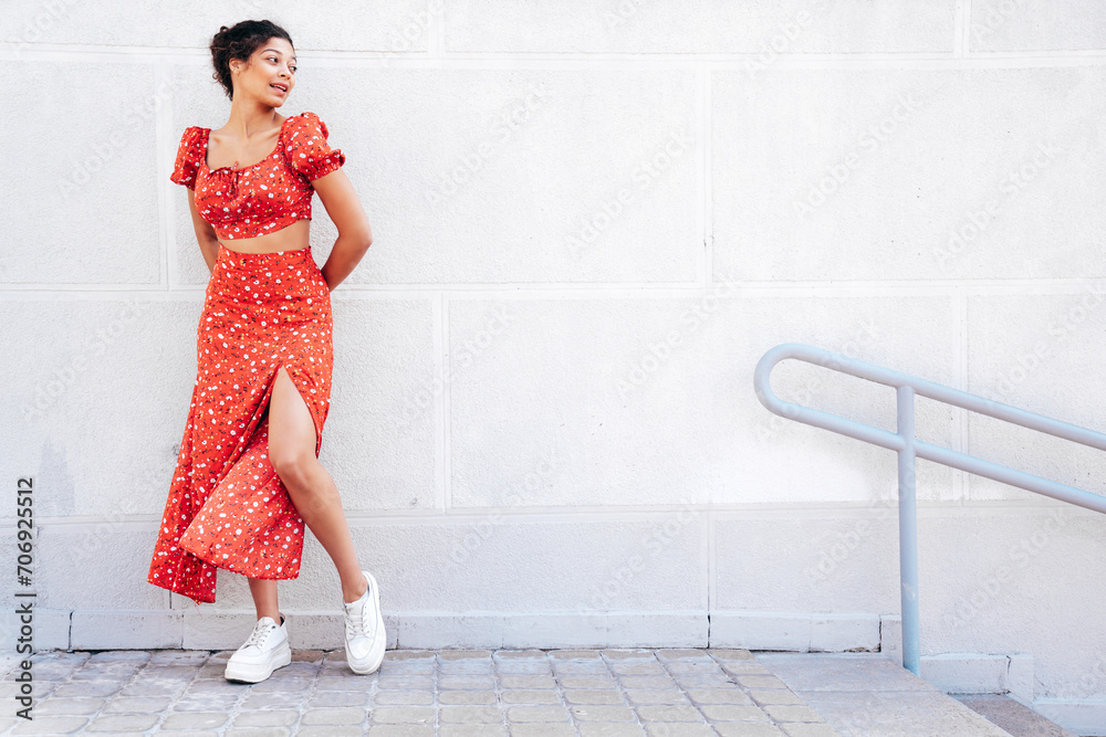 Young beautiful smiling hipster woman in trendy summer red dress. Carefree woman posing in the street near wall. Positive model outdoors in at sunny day. Cheerful and happy Young beautiful smiling hipster woman in trendy summer red dress. Carefree woman posing in the street near wall. Positive model outdoors in at sunny day. Cheerful and happy