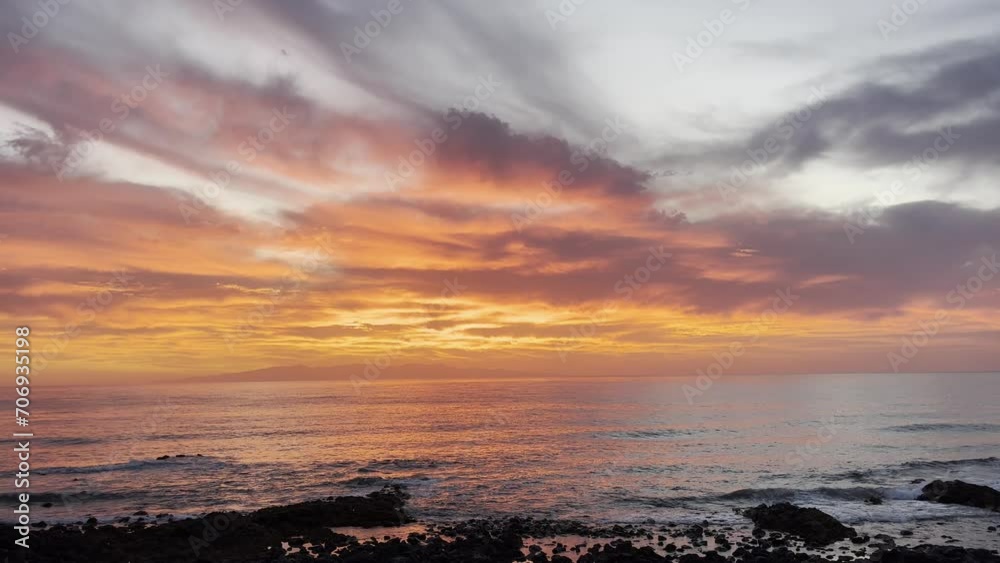 Wonderful red orange sunset on the ocean horizon with island in background. Colorful amazing sky with clouds and calm sea shore view. Tourism and travel journey scenic destination.