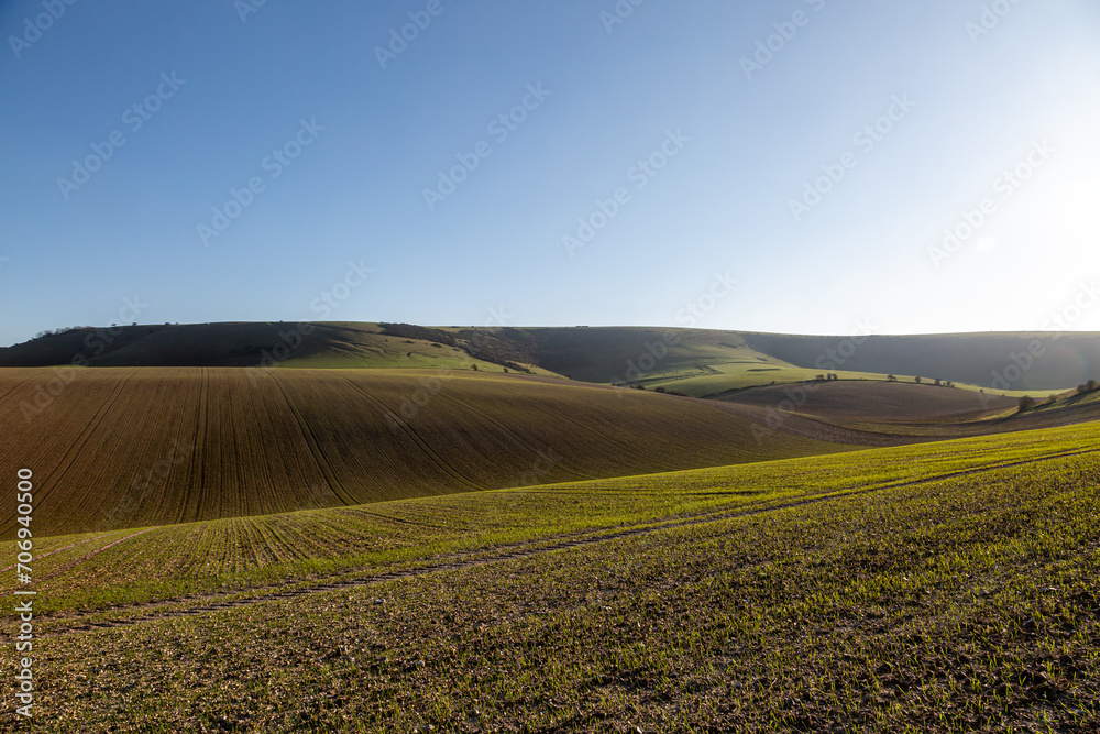 Looking out over fields towards Kingston Ridge in the South Downs, with a blue sky overhead Looking out over fields towards Kingston Ridge in the South Downs, with a blue sky overhead