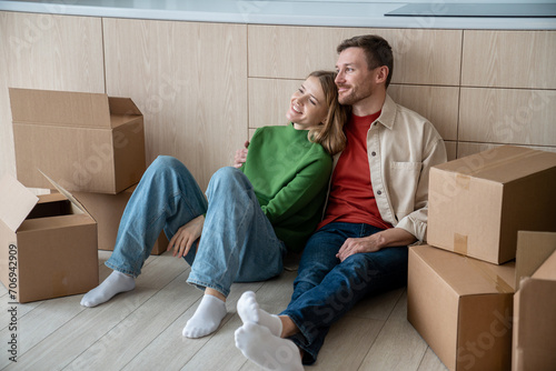 Happy couple man woman hugging dreaming about living in new apartment sitting on floor on kitchen at home. Relocation, moving to flat, family mortgage concept. Spouses enjoying life changes resting. photo