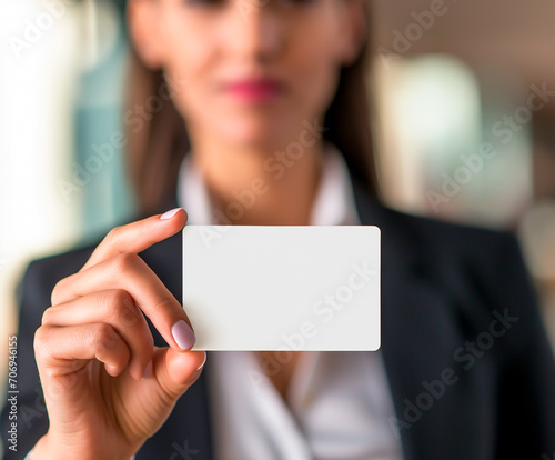 Career woman in a suit holding a blank white business card, focus on card with copy space.
