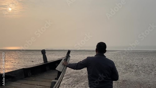 Close up rear shot of a man holding an Indian fishing boat during sunset at a beach in Bengal , India. photo