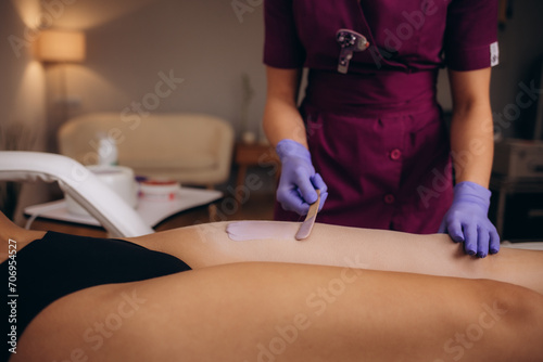 A master applies pink depilatory wax to a young woman's leg for hair removal. Depilation with wax. Beauty concept. Place for text. Selective focus. photo