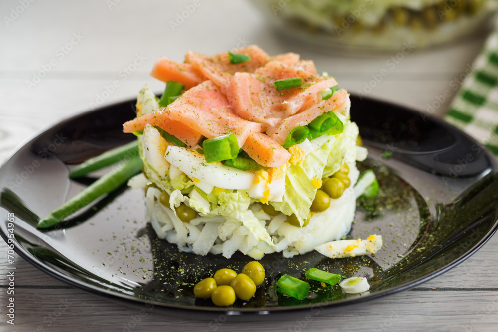 Layered salad of cabbage and other vegetables with pieces of red fish in a plate. Layered salad of cabbage and other vegetables with pieces of red fish in a plate.