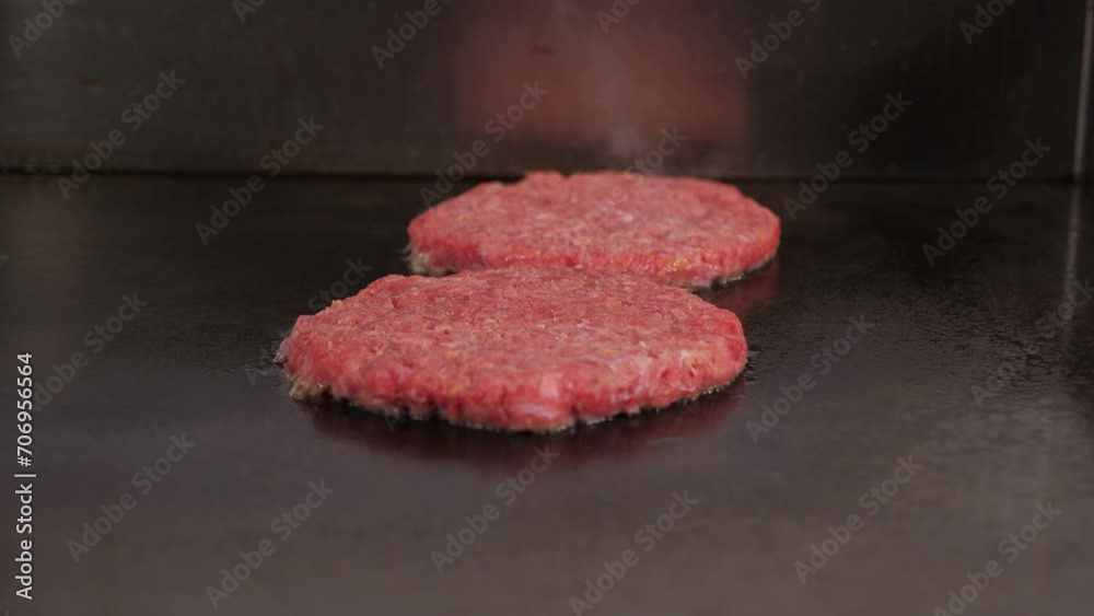 Close-up of two juicy burger patties fried on an industrial chain in a restaurant kitchen, bubbles of boiling oil and smoke from frying juicy patties. Close-up of two juicy burger patties fried on an industrial chain in a restaurant kitchen, bubbles of boiling oil and smoke from frying juicy patties.