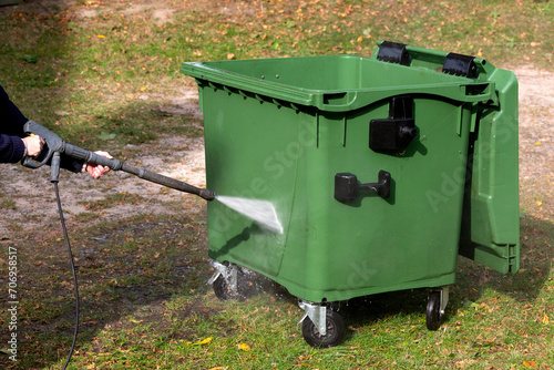 A municipal service worker treats a garbage container with a disinfectant solution. Washing the garbage container.