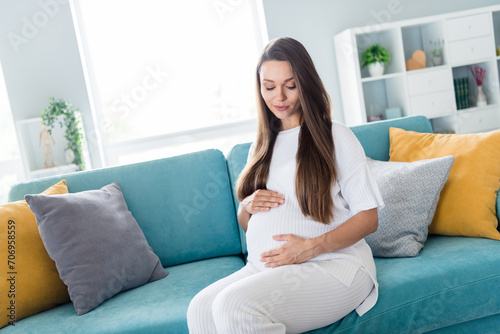 Photo of gentle dreamy woman pregnant girl sitting on comfy couch touching belly enjoying the moment