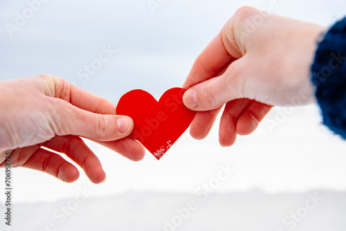 Hands holding red heart on winter background.