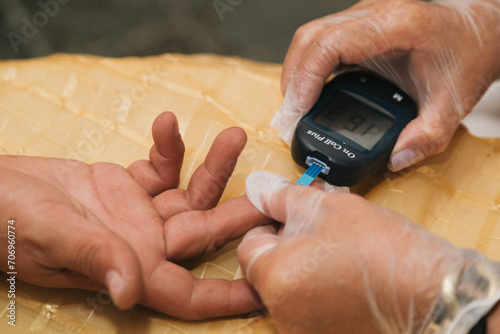 Person wearing gloves taking a blood sample from a patient's finger to test their glucose levels.