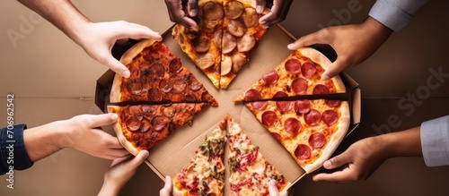 Seen from above, several human hands are holding pizza on a newly opened pizza carton