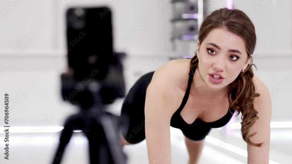 An athletic young woman is doing an online workout in the fitness room. Sports blogger, fitness and yoga teacher, online class, health coach An athletic young woman is doing an online workout in the fitness room. Sports blogger, fitness and yoga teacher, online class, health coach