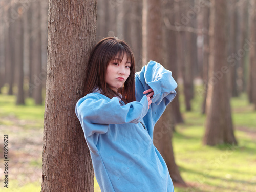 Beautiful young Chinese woman posing in sunny summer forest, wearing blue loose oversized top and miniskirt with small shoulder bag. Emotions, people, beauty, youth and lifestyle portrait. photo