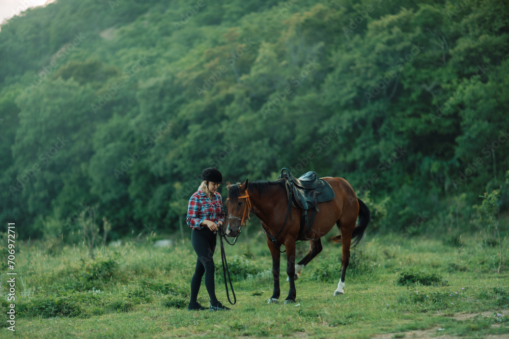 Happy blonde with horse in forest. Woman and a horse walking through the field during the day. Dressed in a plaid shirt and black leggings.