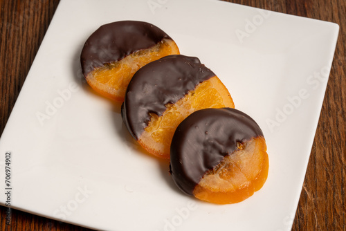 Three orange slices are dipped in dark chocolate are served on a white plate.