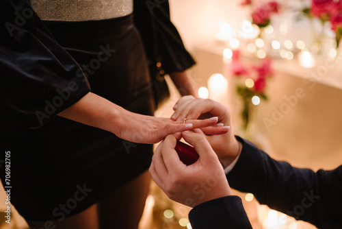 Engagement ring. Man in love putting a ring on woman finger. Propose. Closeup hands. Offer of hand and heart. Man making a marriage proposal to his woman. Engaged couple in Valentine s Day evening.