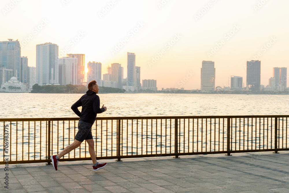 Man running on sea bay front. Man jog on seaside, enjoying beautiful morning city.