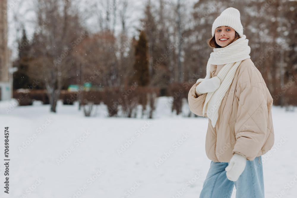 Obraz premium Young adult caucasian woman dressed coat scarf hat and mittens enjoys winter weather at white snowy winter park