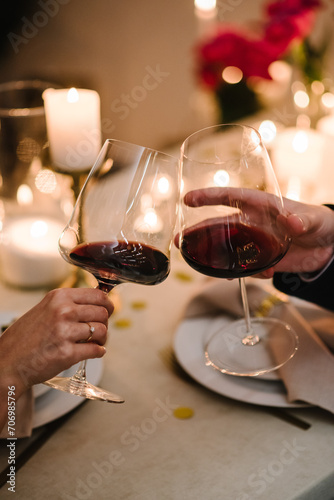 Cheers. Romantic date by candlelight at night. Couple in love drinking wine. Hands man and woman hold glasses at home. Toast. Dinner setup table for couple on Valentine's day. Proposal hand and heart.
