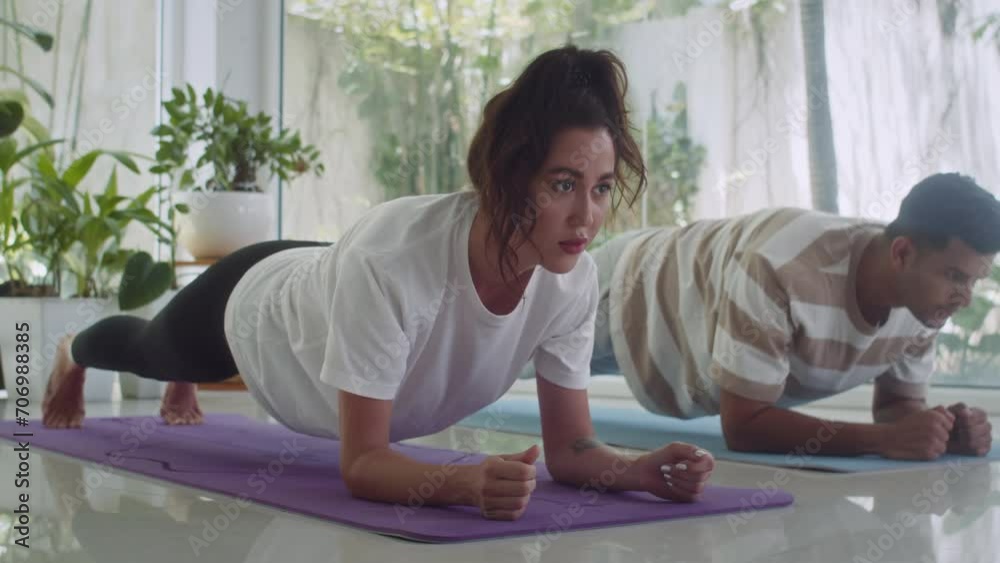 Medium long shot of young girl and her boyfriend practicing plank exercise on floor while working out at home