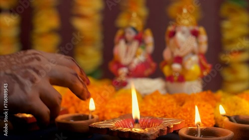 Indian woman hand placing diya in front of Hindu Gods - Diwali  idol worship  festival of lights  religious ritual. Family preparing for Deepawali puja - colorful flowers  Lord Ganesh  Devi Laxmi  ... photo