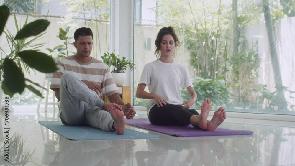 Long shot of biracial sportspeople in activewear doing leg warm up before yoga class sitting on mat on floor at home Long shot of biracial sportspeople in activewear doing leg warm up before yoga class sitting on mat on floor at home