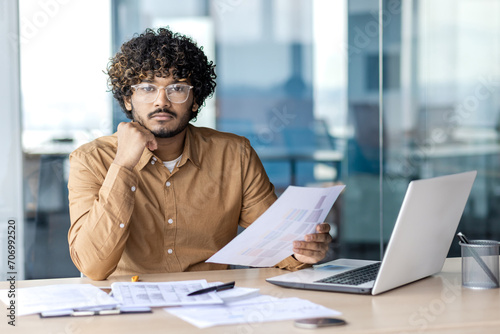 Photos Portrait of serious concentrated businessman inside office, man looking at camera holding papers financial reports, accountant financier with laptop on paper work