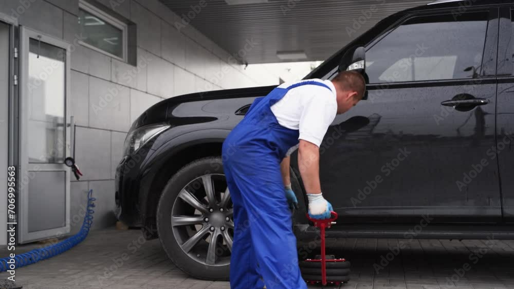 Auto mechanic uses pneumatic air jack to lift SUV, removes tire with impact wrench in garage. Workshop professional, vehicle maintenance, tire change, car service, repairman in uniform at work. Auto mechanic uses pneumatic air jack to lift SUV, removes tire with impact wrench in garage. Workshop professional, vehicle maintenance, tire change, car service, repairman in uniform at work.