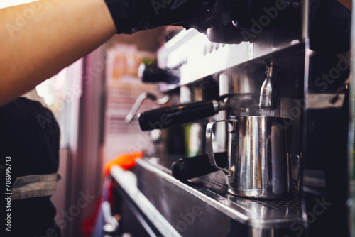 Barista in black gloves presses the button for pouring boiling water into metal cup while preparing coffee drink or cocktail.