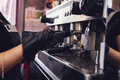Barista in black gloves and apron rinses the holder of automatic coffee machine before preparing the next cup of coffee. photo
