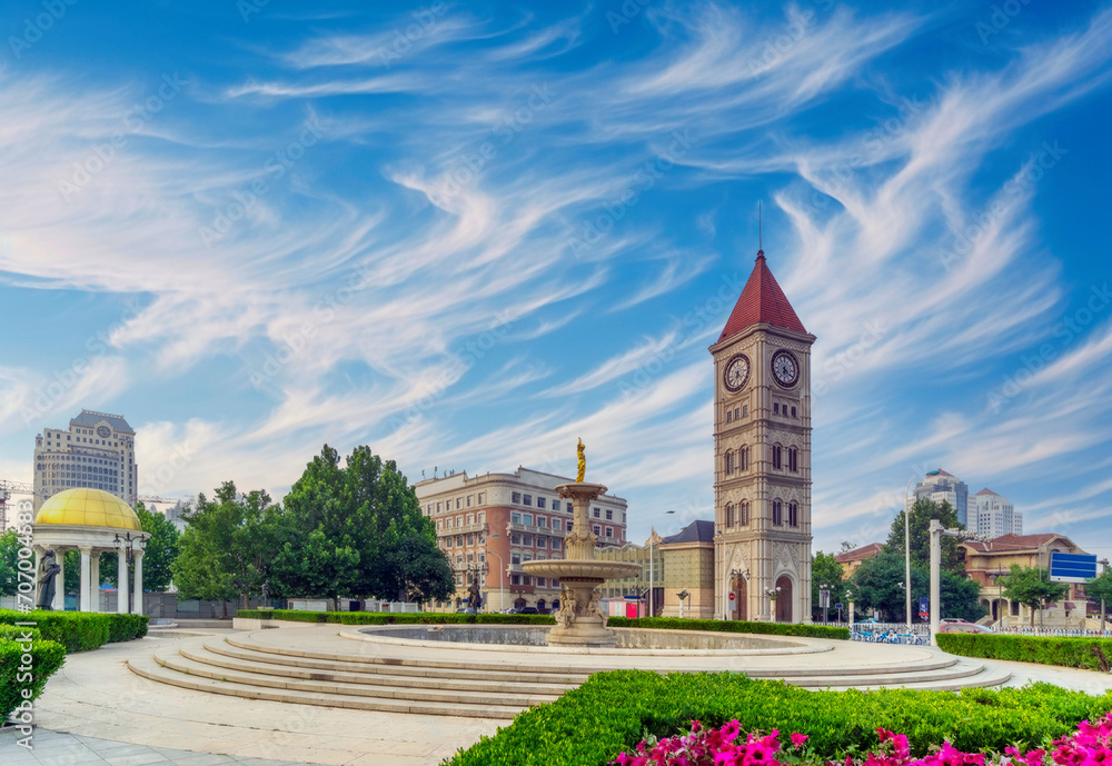 Fototapeta premium European-Inspired Clock Tower in City Square with Yellow Dome Pavilion, Manicured Greenery, and Dynamic Sky