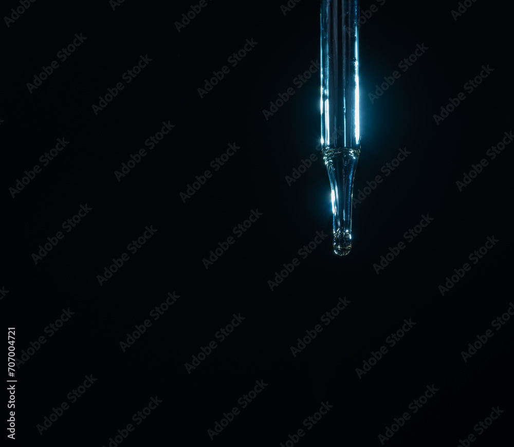 Glass pipette for cosmetics. A drop of cosmetics oil on a black background close-up macro Glass pipette for cosmetics. A drop of cosmetics oil on a black background close-up macro